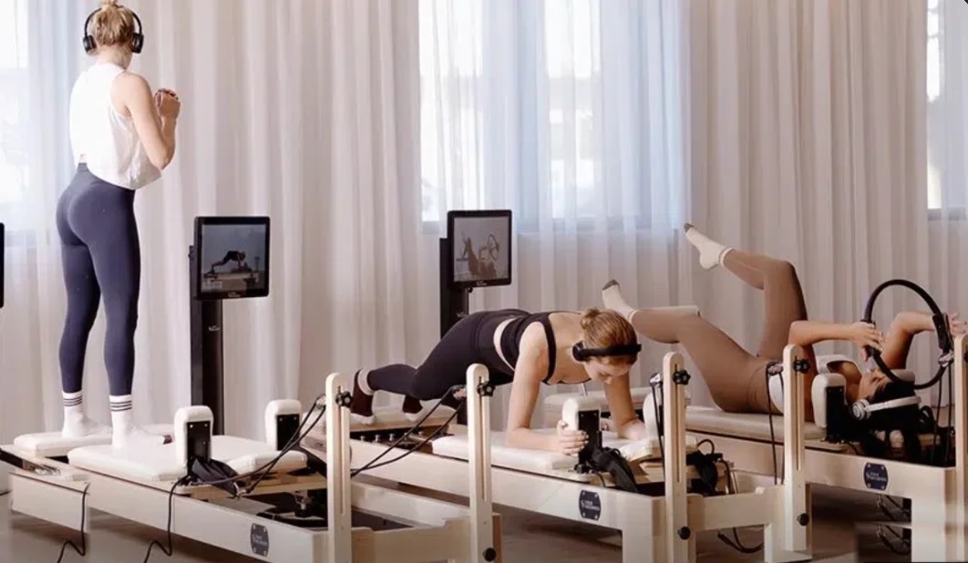 Reformer Pilates Studio: drei Frauen trainieren mit Kopfhörern auf Reformern mit Screen
